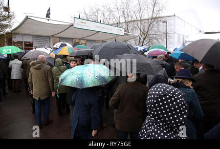 Racegoers abri de la pluie pendant qu'ils attendent pour les portes à ouvrir pour défendre jour de la Cheltenham Festival 2019 à l'Hippodrome de Cheltenham. Banque D'Images