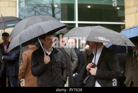 Racegoers abri de la pluie pendant qu'ils attendent pour les portes à ouvrir pour défendre jour de la Cheltenham Festival 2019 à l'Hippodrome de Cheltenham. Banque D'Images