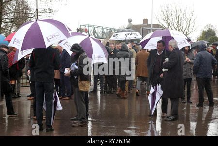 Racegoers abri de la pluie pendant qu'ils attendent pour les portes à ouvrir pour défendre jour de la Cheltenham Festival 2019 à l'Hippodrome de Cheltenham. Banque D'Images