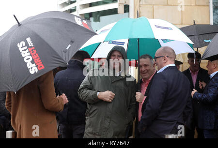 Racegoers abri de la pluie pendant qu'ils attendent pour les portes à ouvrir pour défendre jour de la Cheltenham Festival 2019 à l'Hippodrome de Cheltenham. Banque D'Images