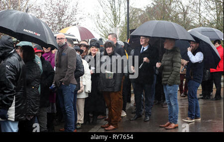 Racegoers abri de la pluie pendant qu'ils attendent pour les portes à ouvrir pour défendre jour de la Cheltenham Festival 2019 à l'Hippodrome de Cheltenham. Banque D'Images