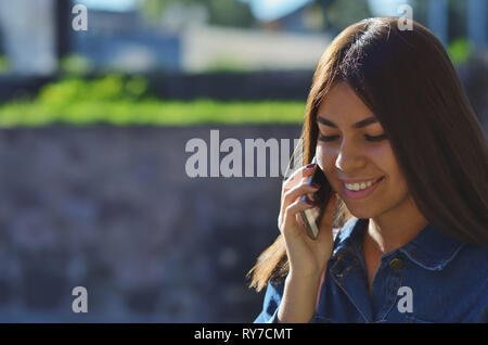 Portrait d'une jeune fille attirante qui parle au téléphone dans la rue et de sourires Banque D'Images