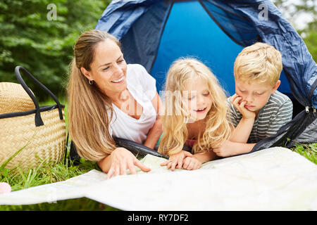 Les enfants des frères et sœurs et de la mère dans la tente regarder curieusement sur une carte Banque D'Images
