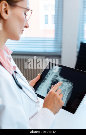Doctor looking at x-ray photo d'une épaule sur sa tablet computer Banque D'Images