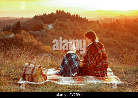 La mère et l'enfant moderne heureux dans l'avant de paysages de Toscane sur le coucher du soleil assis sur la couverture et à la recherche sur l'autre. Banque D'Images