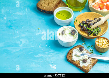 Le fromage à la crème sur une tranche de pain garni, bol de fromage à la crème, mozzarella, pignons et traditionnel grec italien apéritif olives séchées sur bleu conc Banque D'Images