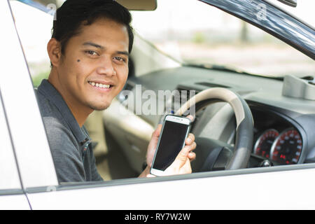 Les jeunes hommes attrayants à l'aide de téléphone mobile et à la caméra à tout en conduisant sa voiture à sunny day Banque D'Images