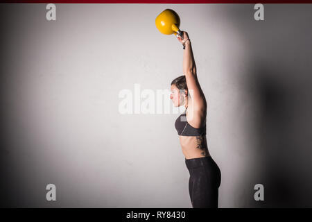 Une jeune femme sportive concentrée dans les vêtements de sport, qui augmente la kettlebell dans la salle de sport Banque D'Images