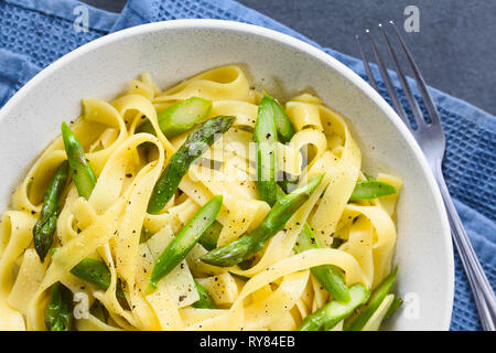 Des pâtes fraîches plat de fettucine ou tagliatelle, asperges vertes, l'ail et le jus de citron dans un bol, de poivre noir sur le dessus Banque D'Images