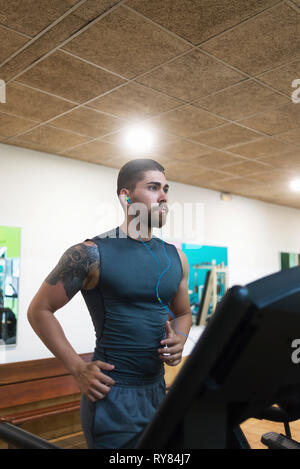 L'homme à l'écoute de la musique tout en s'exécutant sur tapis roulant dans une salle de sport Banque D'Images