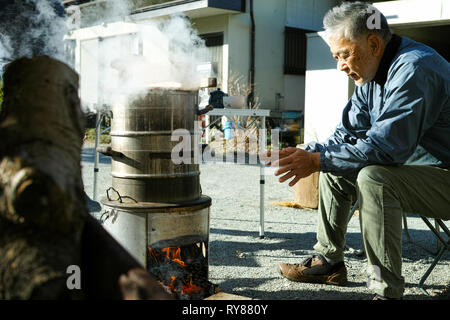 Un ancien homme d'Asie de se réchauffer par le feu de camp Banque D'Images