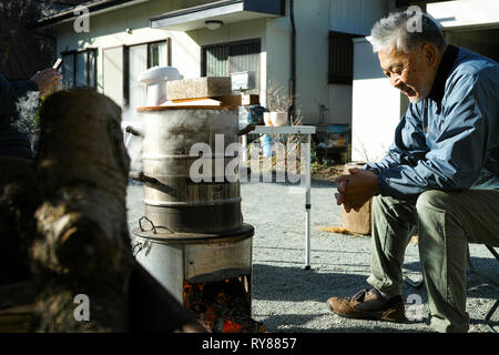 Un ancien homme d'Asie de se réchauffer par le feu de camp, smiling Banque D'Images