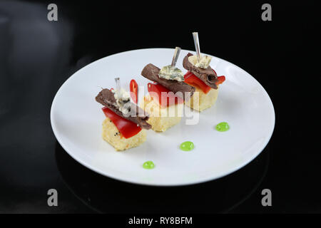 Viandes tranchées, roulé dans un rouleau, des canapés avec du fromage bleu et rouge, sur une brochette, close-up, pour le menu Banque D'Images