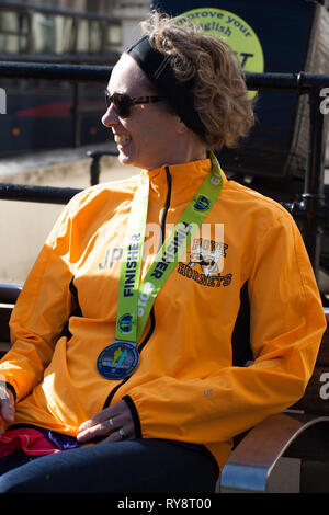 Une femme ( de Hove Harrier ) avec médaille d'or pour compléter le demi-marathon de Brighton le 24 février 2019 ,détente sur mur au côté de Hellenic Gre Banque D'Images