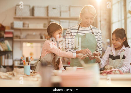 Jusqu'à la taille de l'art portrait enseignant travaillant avec les enfants en classe de poterie théâtre éclairée par la lumière du soleil, copy space Banque D'Images