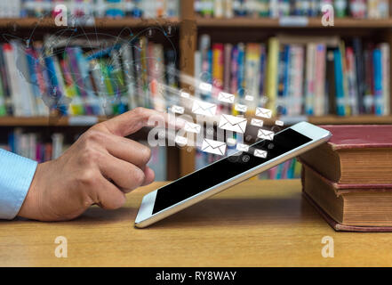 Pointer du doigt sur l'écran de l'ordinateur tablette avec e-mail et ligne de réseau au cours de la table de bois dans la bibliothèque, de l'éducation Technologie concept Banque D'Images