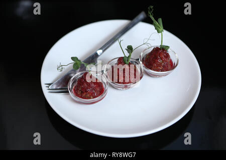 Sauce Tartare délicieux rouge dans trois pialas sur une plaque avec un couteau et une fourchette, décoré avec une tige de pois verts, close-up, pour un restaurant. Banque D'Images