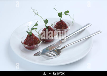 Sauce Tartare délicieux rouge dans trois pialas sur une plaque avec un couteau et une fourchette, décoré avec une tige de pois verts, close-up, pour un restaurant. Banque D'Images