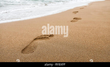 Close up d'empreintes de pas dans le sable humide sur la plage au coucher du soleil. Concept pour se rendre dans des endroits exotiques, tropicaux / locations et vacances. Banque D'Images