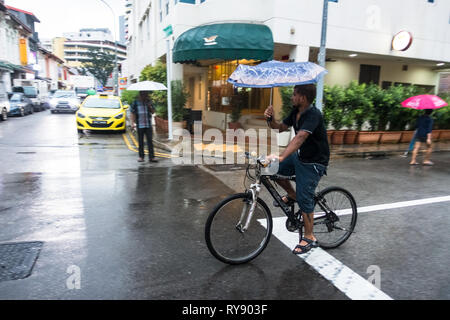 L'homme indien de la bicyclette tout en tenant un parapluie sous la pluie - Little India, Singapour Banque D'Images