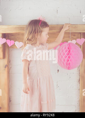 Petite fille en robe rose pastel et bandeau de la couronne ornant le prix avec les pompons, cheminée en bois massif, Teinté d'arrière-plan, selective focus Banque D'Images