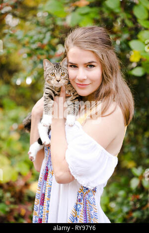 Portrait of smiling woman carrying chat mignon debout contre des plantes en forêt Banque D'Images