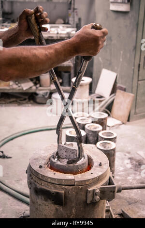 Les mains de mâle avec pinces de levage en tenant de produits métalliques de creuset sur peu de Foundry Banque D'Images