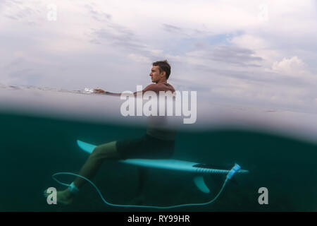 Vue latérale d'homme flottant sur planche de surf dans l'eau azure de mer à Bali, Indonésie Banque D'Images