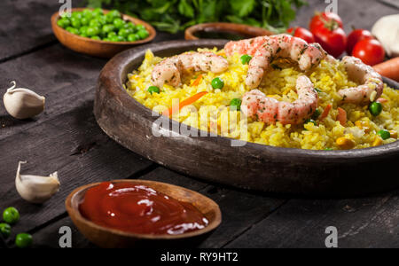 Riz blanc cuit aux crevettes, curry et de légumes dans un plat en bois sur un fond noir. Banque D'Images