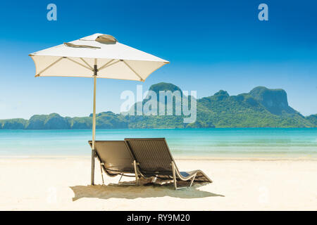 Deux chaises de plage sous un parapluie bleu sur la plage de sable blanc Banque D'Images