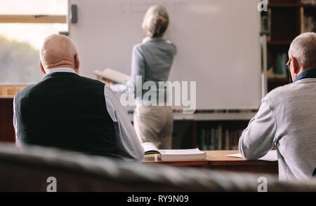 Les hommes participant à une conférence dans une salle de classe. Vue arrière de l'écriture féminine senior lecturer à bord en classe. Banque D'Images