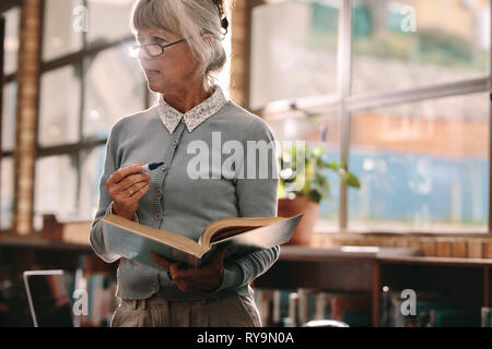 Close up of a senior lecturer standing in classroom tenant un livre et le marqueur. Portrait d'une femme âgée professeur enseignant. Banque D'Images