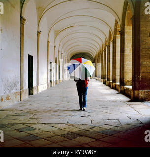 Femme avec parapluie multicolores balade dans les galeries de la place centrale de Marciac, France. Ce village est bien connu en raison de sa consommation de J Banque D'Images