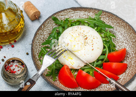 Meubles de cuisine gastronomique italienne burrata fromage servi sur un plateau d'argile brun avec roquette fraîche, des tomates, du poivre et l'huile d'olive avec fourchette et k Banque D'Images