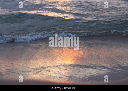 Marcher sur la plage et regarder le coucher du soleil. Sentir les vagues tour doucement à vos pieds et chevilles après une journée calme. Le sable en laissant des impressions. Banque D'Images