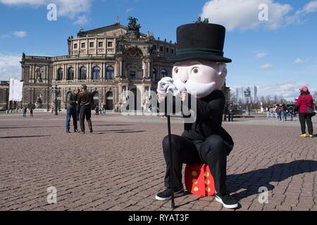 Dresde, Allemagne. Mar 13, 2019. Un homme dans un costume par monsieur Monopoly, la mascotte de l'American Board game, est assise sur un cube de mousse en face de l'Opéra Semper lors d'une conférence de presse. À la fin de 2019, le "monopole" de l'édition de Dresde jeu de société sera lancé. Credit : Sebastian Kahnert/dpa-Zentralbild/dpa/Alamy Live News Banque D'Images