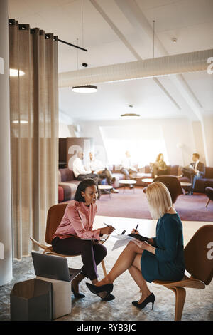Deux jeunes femmes d'assis dans des chaises ensemble dans un bureau moderne discussing paperwork lors d'une réunion Banque D'Images