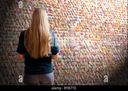 Femme blonde aux cheveux longs, debout devant un mur avec beaucoup de gens des visages, social media concept Banque D'Images