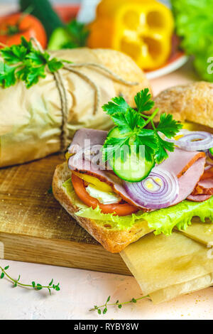 Sandwich Ciabatta au jambon, tomates, fromage, poivre, l'oignon et la salade sur planche à découper en bois avec des ingrédients. Banque D'Images