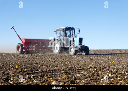 Tracteur bleu avec un semoir rouge travaille sur le terrain par un beau jour d'automne ensoleillé Banque D'Images