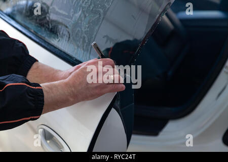 L'assistant d'installation d'équipement supplémentaire bois une teinte film sur le côté de la vitre avant de la voiture et l'arrêt de la partie excédentaire à l'aide d'un couteau Banque D'Images