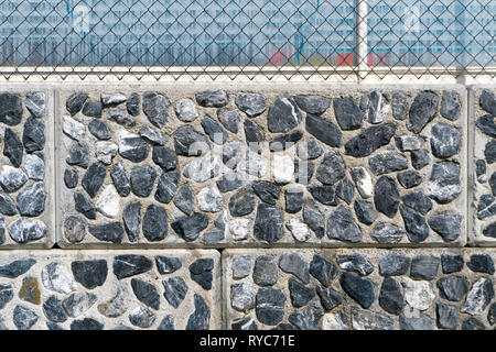 Détail horizontal d'un mur de roche contexte constitué de petites pierres de granit déchiquetés par les carreaux et les joints de coulis et une clôture sur le dessus Banque D'Images