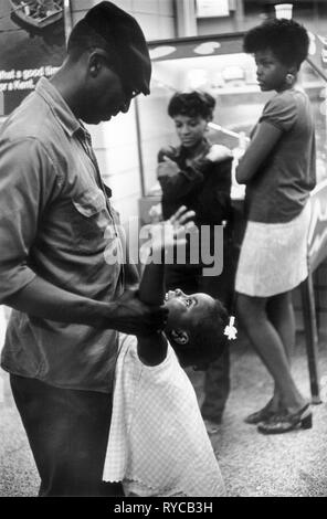 Le père et la fille afro-américains des années 60 jouent ensemble tandis que les sœurs plus âgées se penchent contre une machine à balles à broche. Tard dans la nuit dans une gare routière Greyhound Washington DC États-Unis 60s. HOMER SYKES Banque D'Images