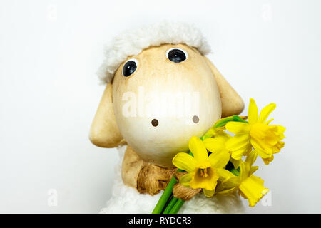 Pâques mignon jouet mouton narcisses holding bouquet de jonquilles dans sa main avec un fond blanc Banque D'Images