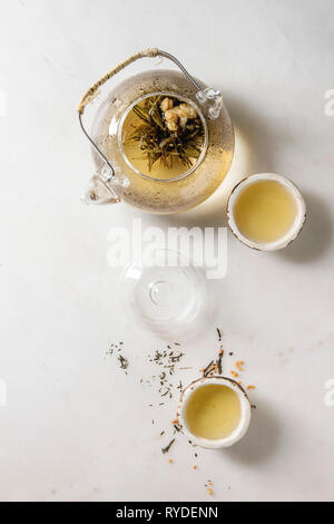 Thé vert chaud dans deux chinois traditionnels et tasse en céramique argile théière en verre sur fond de marbre blanc. Mise à plat, de l'espace Banque D'Images