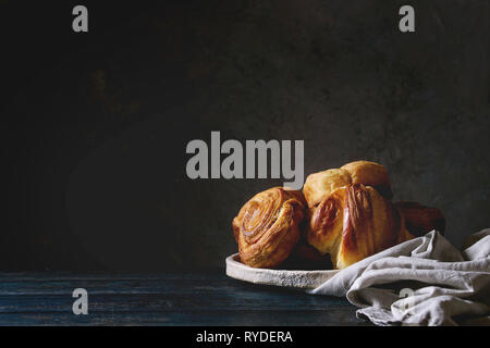 Variété de pâte feuilletée faite maison à la cannelle brioches et croissants dans la plaque en céramique sur table en bois. La vie encore sombre. Copy space Banque D'Images