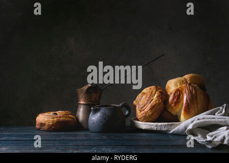 Variété de pâte feuilletée faite maison à la cannelle brioches et croissants servis avec vintage coffee pot sur table en bois. La vie encore sombre. Copy space Banque D'Images