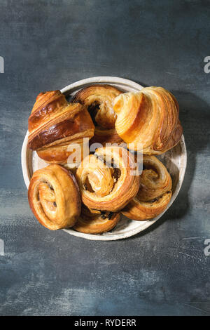 Variété de pâte feuilletée faite maison à la cannelle brioches et croissants servis dans une plaque en céramique bleu sur fond de texture. Mise à plat, de l'espace Banque D'Images