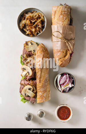 Ouvert et attaché avec sandwich baguette boeuf champignon champignons, salade verte, oignon frit avec des ingrédients dans des bols sur fond de marbre blanc. Fla Banque D'Images