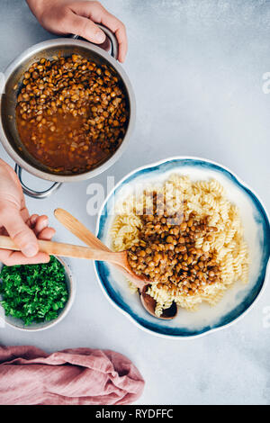 Woman pouring lentilles vertes cuites sur les pâtes cuites dans un bol. Banque D'Images
